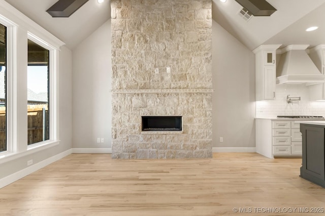 unfurnished living room with light wood finished floors, a fireplace, visible vents, and vaulted ceiling