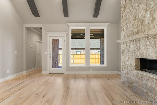 unfurnished living room featuring ceiling fan, a stone fireplace, baseboards, and wood finished floors