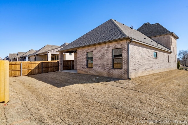 back of property featuring a patio, brick siding, roof with shingles, and fence