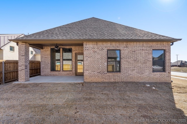 rear view of house with ceiling fan, a patio, brick siding, fence, and roof with shingles