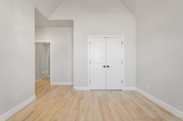 unfurnished bedroom with light wood-style flooring, baseboards, vaulted ceiling, and a closet