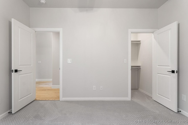 unfurnished bedroom with a spacious closet, a closet, carpet, and baseboards