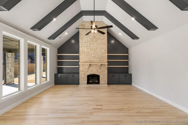 unfurnished living room featuring beamed ceiling, an outdoor stone fireplace, wood finished floors, and baseboards