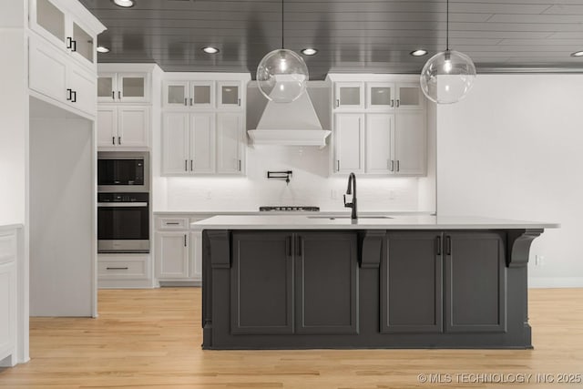 kitchen with a sink, white cabinetry, light countertops, appliances with stainless steel finishes, and light wood finished floors