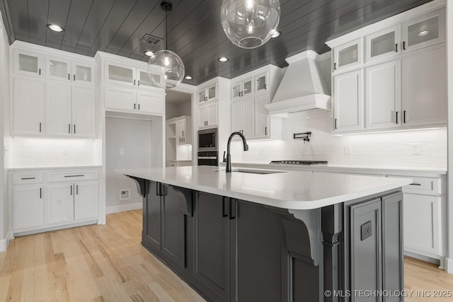 kitchen with wood ceiling, stainless steel microwave, wall chimney range hood, white cabinetry, and a sink