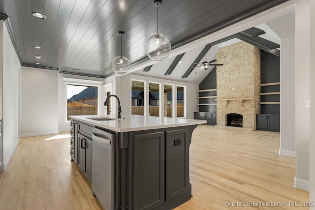 kitchen featuring built in shelves, lofted ceiling, light wood-style floors, a sink, and a stone fireplace