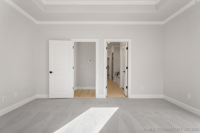 unfurnished bedroom featuring a raised ceiling, ornamental molding, carpet flooring, and baseboards