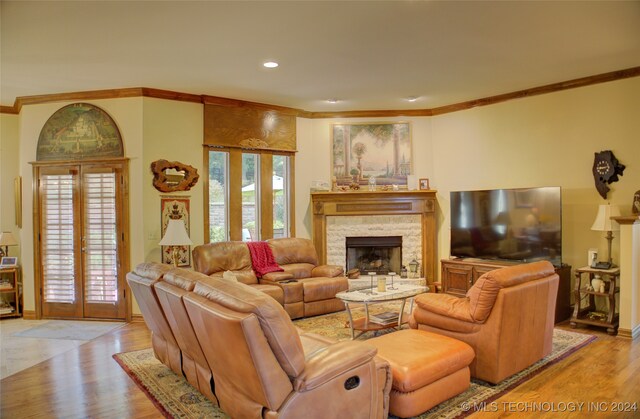 living room featuring ornamental molding, a stone fireplace, french doors, and light hardwood / wood-style floors