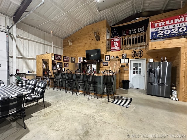 interior space featuring bar, concrete flooring, high vaulted ceiling, and wooden walls