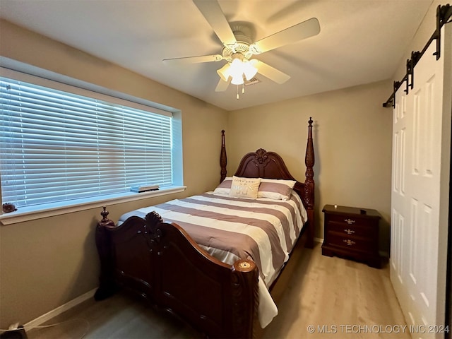 bedroom featuring a barn door, ceiling fan, and light hardwood / wood-style flooring