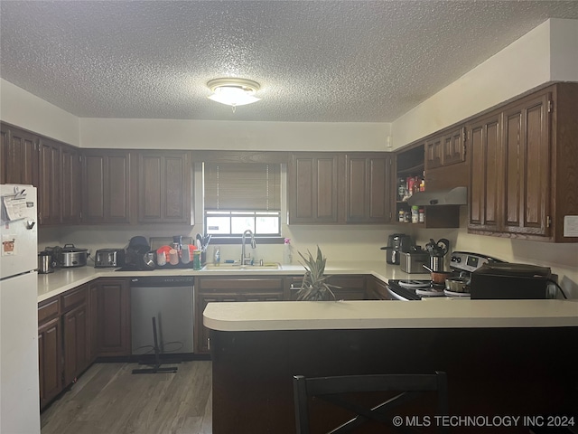 kitchen with stainless steel appliances, dark hardwood / wood-style flooring, dark brown cabinets, kitchen peninsula, and exhaust hood