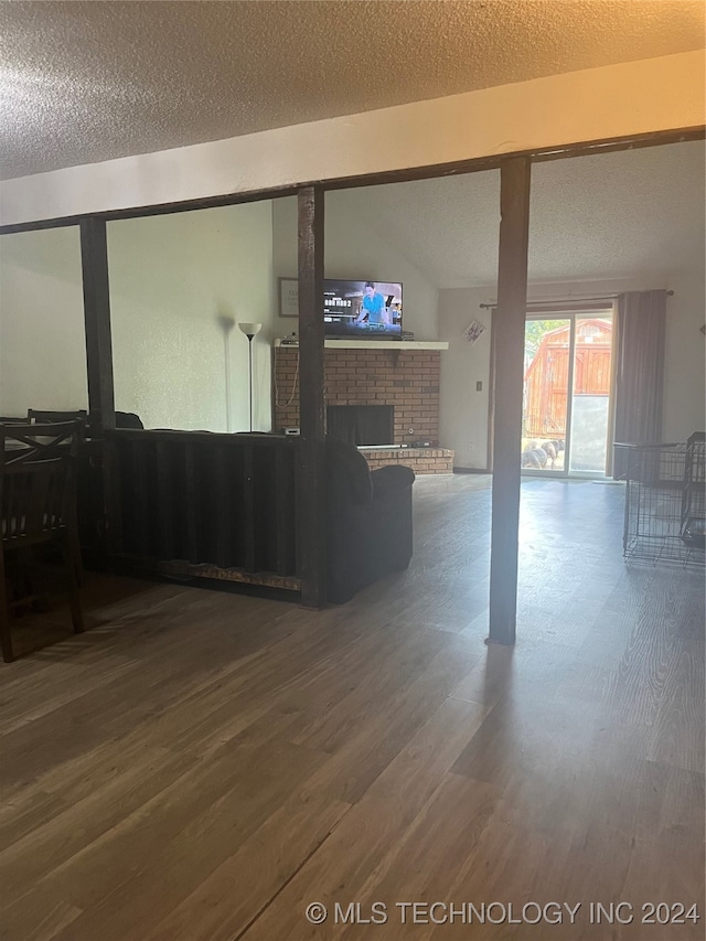 unfurnished room featuring a textured ceiling, wood-type flooring, and a brick fireplace