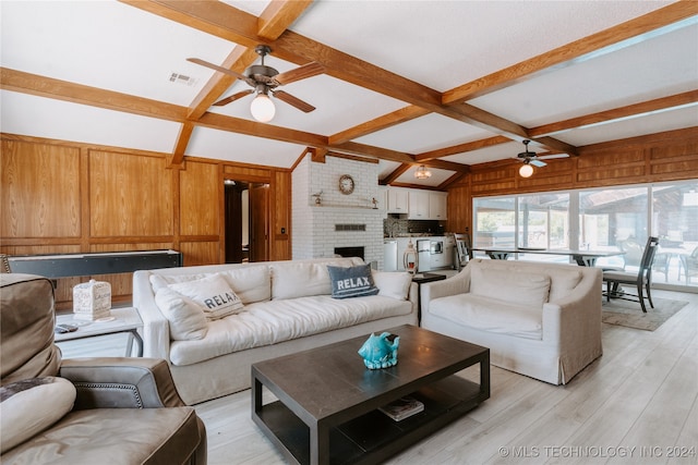 living room featuring a fireplace, beamed ceiling, light wood-type flooring, ceiling fan, and wooden walls