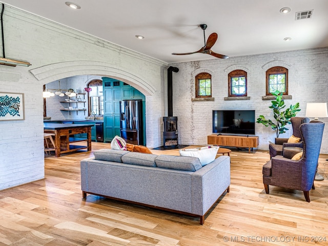 living room with light hardwood / wood-style flooring, a wood stove, crown molding, and ceiling fan