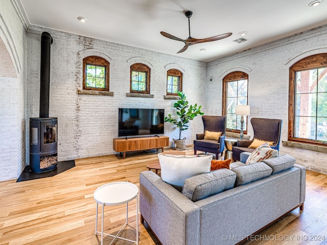 living room featuring brick wall, wood-type flooring, a wood stove, and ceiling fan