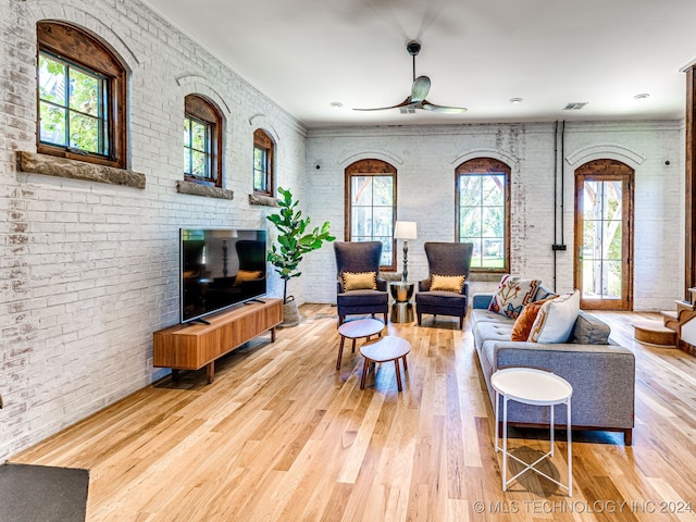 living room featuring brick wall, light hardwood / wood-style floors, a healthy amount of sunlight, and ceiling fan