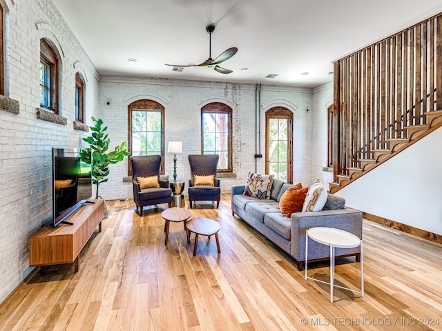 living room with ceiling fan, brick wall, and light wood-type flooring