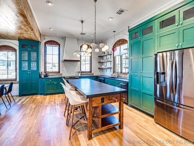 kitchen with sink, stainless steel fridge, pendant lighting, crown molding, and light hardwood / wood-style flooring