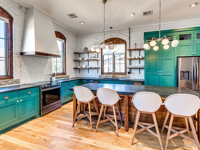 kitchen with wall chimney range hood, hanging light fixtures, a kitchen bar, light wood-type flooring, and stainless steel appliances