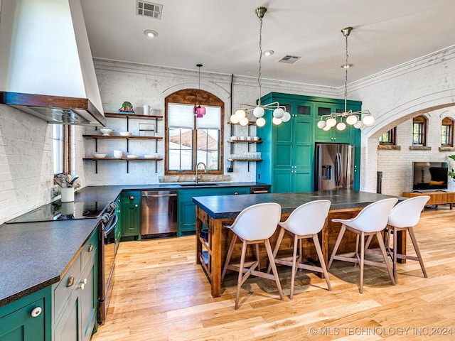 kitchen featuring wall chimney exhaust hood, green cabinets, stainless steel appliances, crown molding, and light wood-type flooring