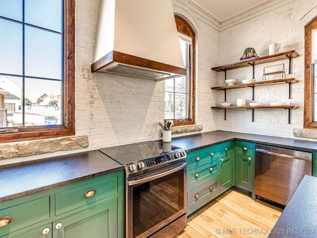 kitchen featuring appliances with stainless steel finishes, crown molding, brick wall, light hardwood / wood-style flooring, and premium range hood