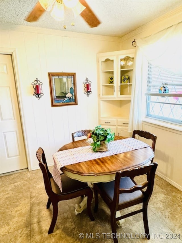 tiled dining space featuring ceiling fan, ornamental molding, and a textured ceiling