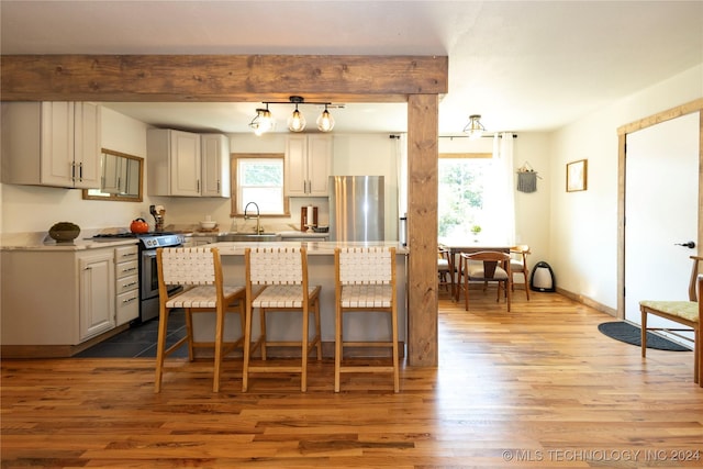 kitchen featuring appliances with stainless steel finishes, beamed ceiling, light wood-style floors, a kitchen bar, and a sink