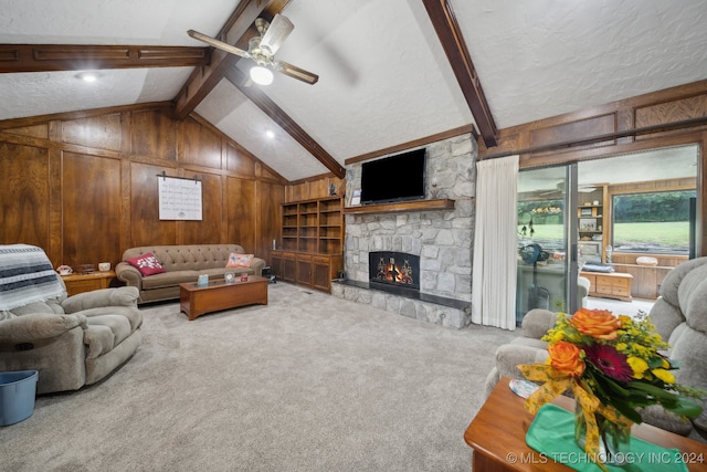 living room featuring wood walls, carpet floors, vaulted ceiling with beams, a stone fireplace, and ceiling fan