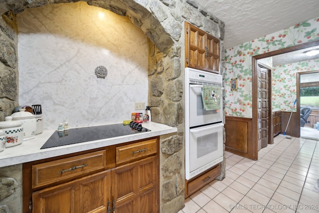 kitchen with white double oven, black electric stovetop, a textured ceiling, and light tile patterned floors