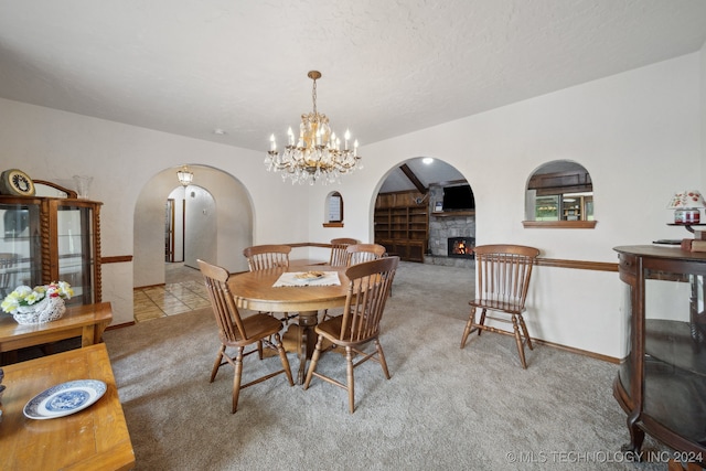 dining room with light carpet, a stone fireplace, and an inviting chandelier