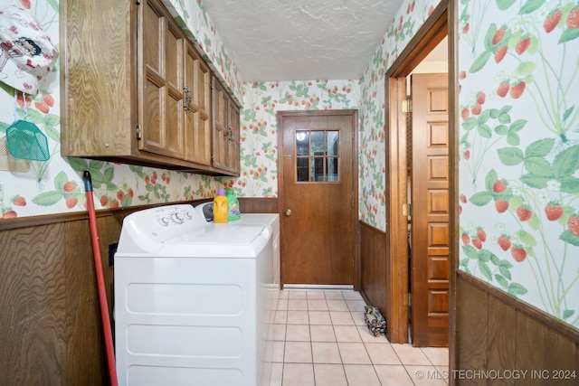 laundry room featuring light tile patterned flooring, a textured ceiling, wooden walls, cabinets, and washer and dryer