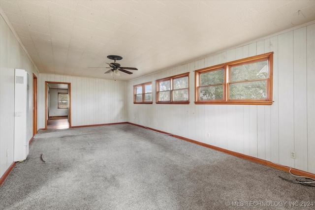 empty room with wooden walls, ceiling fan, and carpet floors