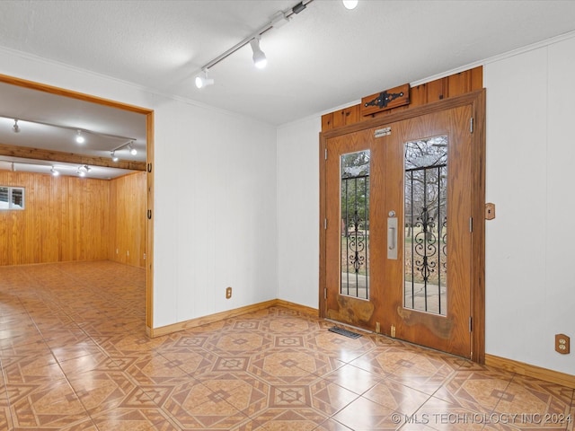 tiled spare room with french doors, rail lighting, a textured ceiling, crown molding, and wooden walls