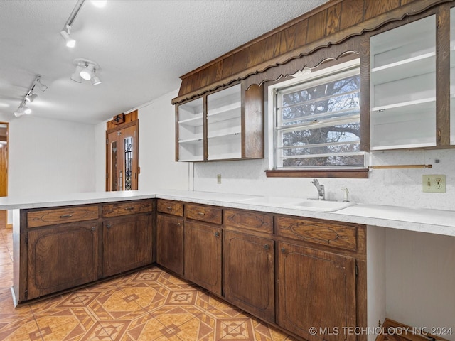 kitchen featuring kitchen peninsula, tasteful backsplash, a textured ceiling, dark brown cabinetry, and sink