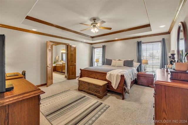 carpeted bedroom with a tray ceiling, connected bathroom, crown molding, and ceiling fan