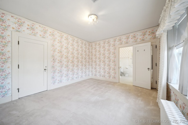 unfurnished room featuring radiator and light colored carpet