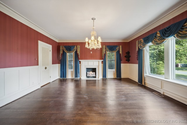 unfurnished living room with a notable chandelier, crown molding, plenty of natural light, and dark hardwood / wood-style flooring