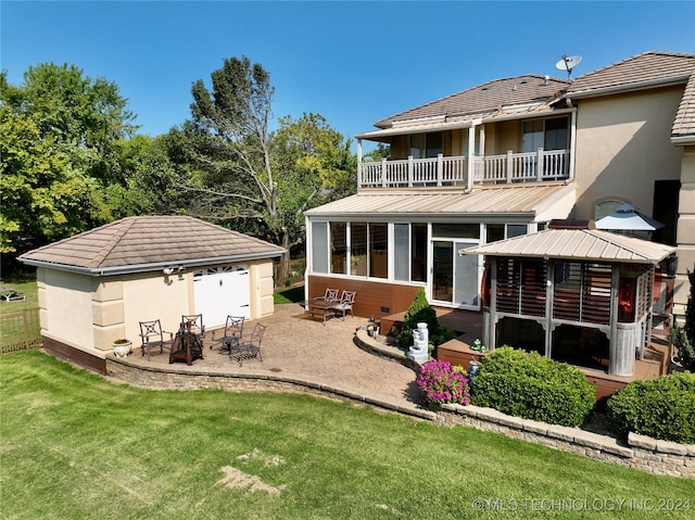 back of property with a balcony, a patio area, a yard, an outdoor structure, and a garage