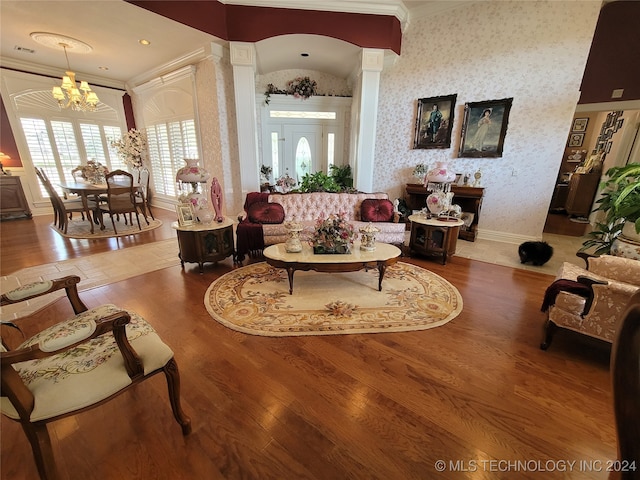 living room featuring crown molding, an inviting chandelier, vaulted ceiling, hardwood / wood-style flooring, and ornate columns