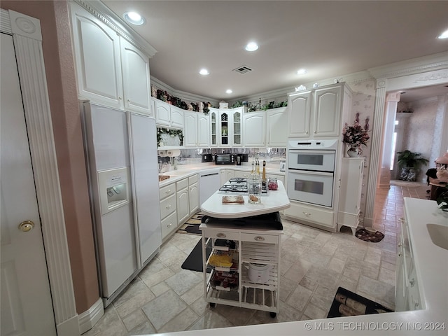 kitchen with a kitchen island, backsplash, white appliances, and white cabinets