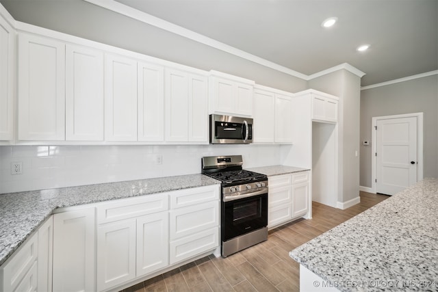 kitchen featuring light wood-type flooring, crown molding, white cabinetry, stainless steel appliances, and light stone counters