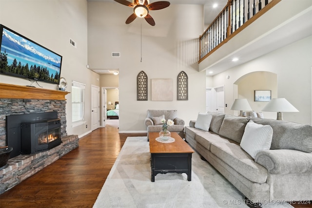 living room with hardwood / wood-style floors, ceiling fan, a stone fireplace, and a towering ceiling