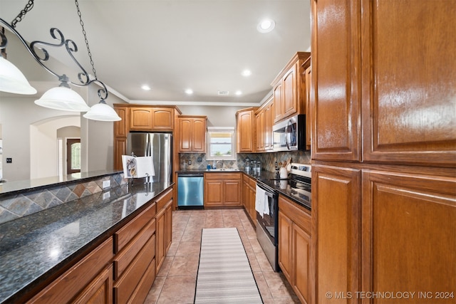 kitchen featuring appliances with stainless steel finishes, backsplash, dark stone counters, sink, and hanging light fixtures