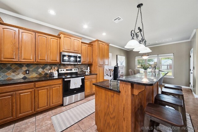 kitchen with decorative backsplash, appliances with stainless steel finishes, ornamental molding, light tile patterned floors, and a kitchen island