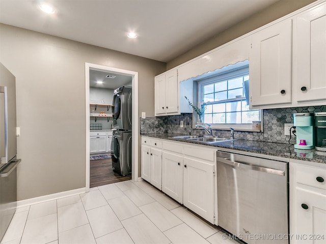 kitchen with stacked washer and clothes dryer, dishwasher, sink, white cabinetry, and dark stone countertops