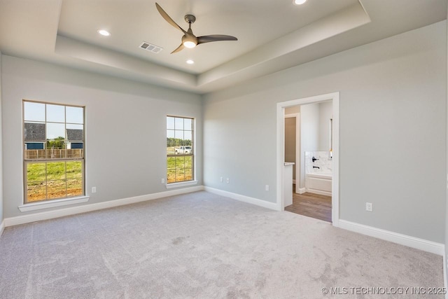 unfurnished bedroom with light colored carpet, a raised ceiling, ceiling fan, and ensuite bathroom