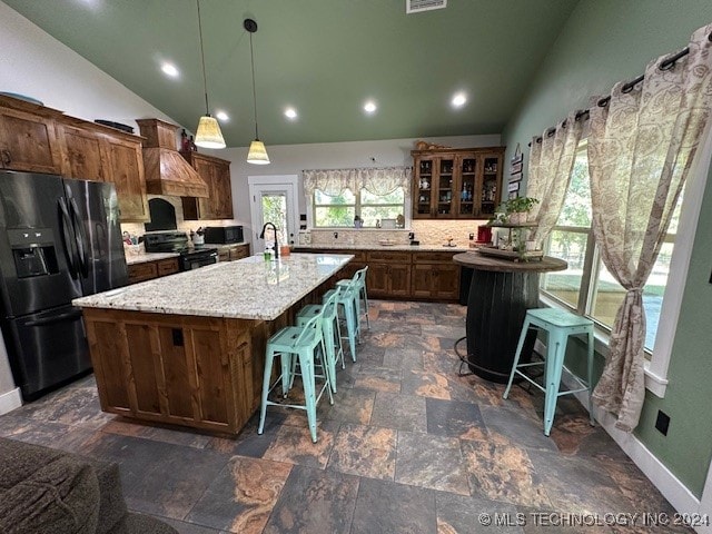 kitchen with black range, pendant lighting, fridge with ice dispenser, an island with sink, and a breakfast bar