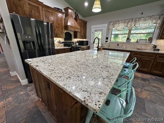 kitchen with a center island with sink, black appliances, a kitchen breakfast bar, and light stone countertops