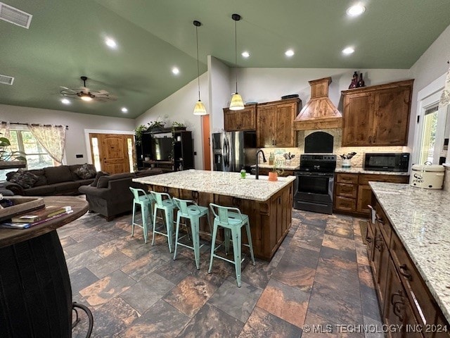 kitchen with a kitchen island with sink, custom exhaust hood, a kitchen breakfast bar, black appliances, and light stone counters