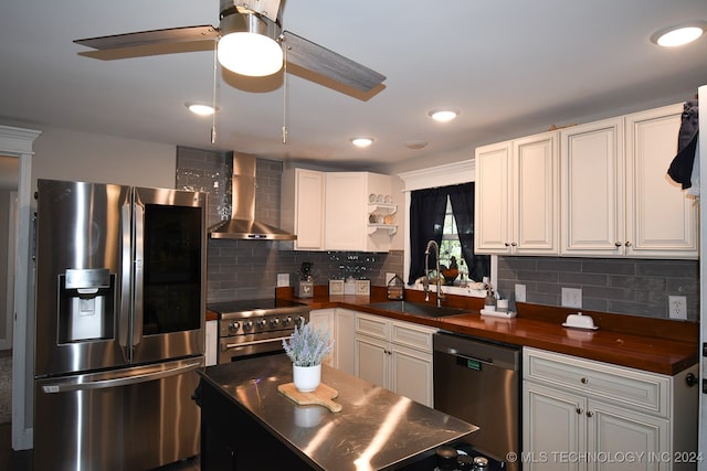 kitchen featuring tasteful backsplash, stainless steel appliances, sink, ceiling fan, and wall chimney range hood